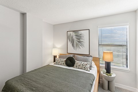 A bedroom with a bed, two lamps, and a framed picture on the wall.