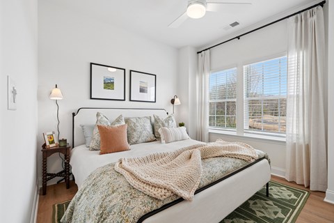 A bedroom with a bed, two lamps, a window, and pictures on the wall.