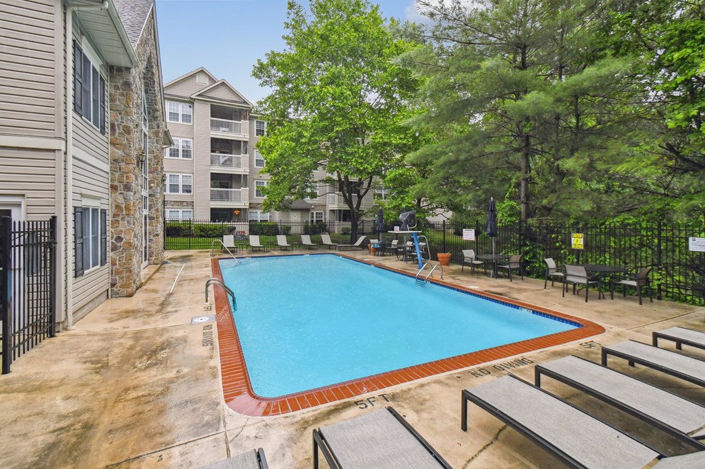 A pool surrounded by trees and chairs.