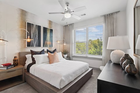 A bedroom with a large bed, a ceiling fan, and a painting on the wall.