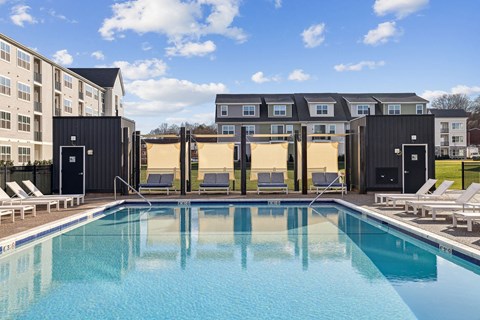 A swimming pool in front of a building with sun loungers on the side.