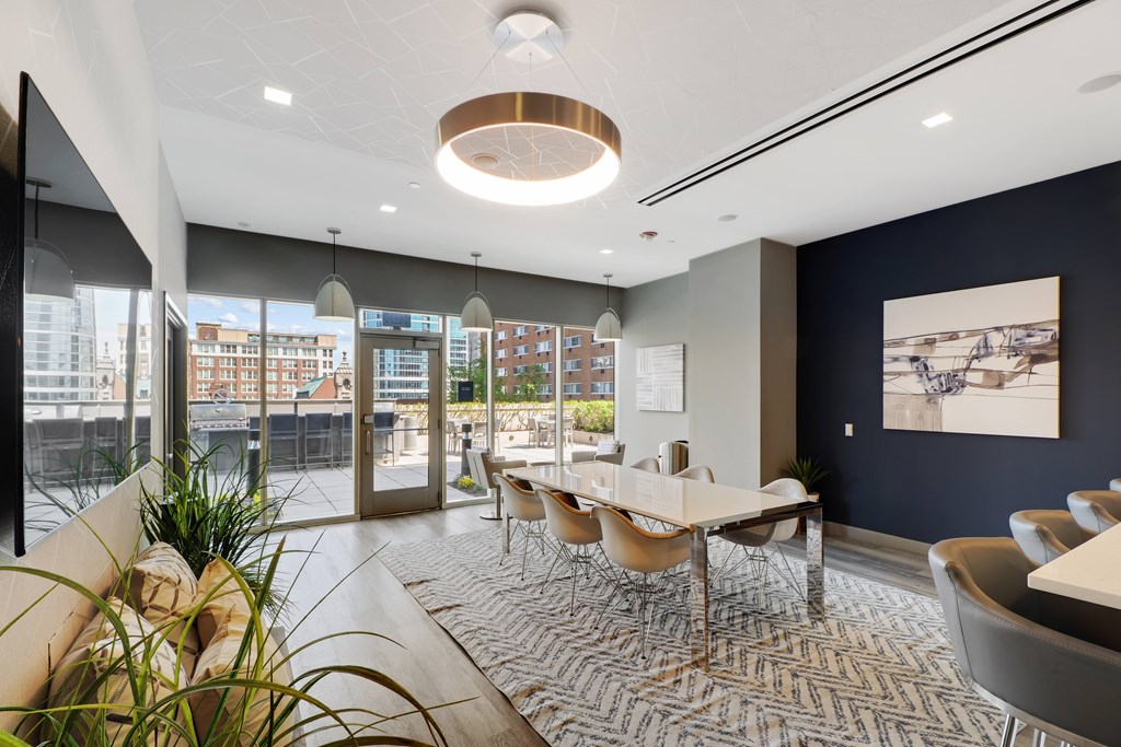 A modern conference room with a long table and chairs, a potted plant, and a view of the city outside the windows.