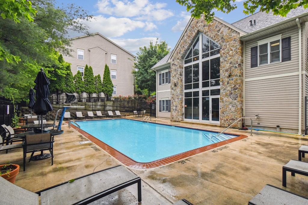 A pool surrounded by a patio and a stone building.