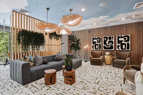 A modern living room with a grey sofa, wooden chairs, and a large hanging light fixture.