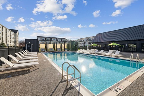 A pool with sun loungers and a building in the background.