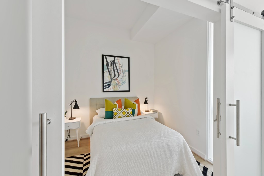 A bedroom with a white bed and a picture on the wall.