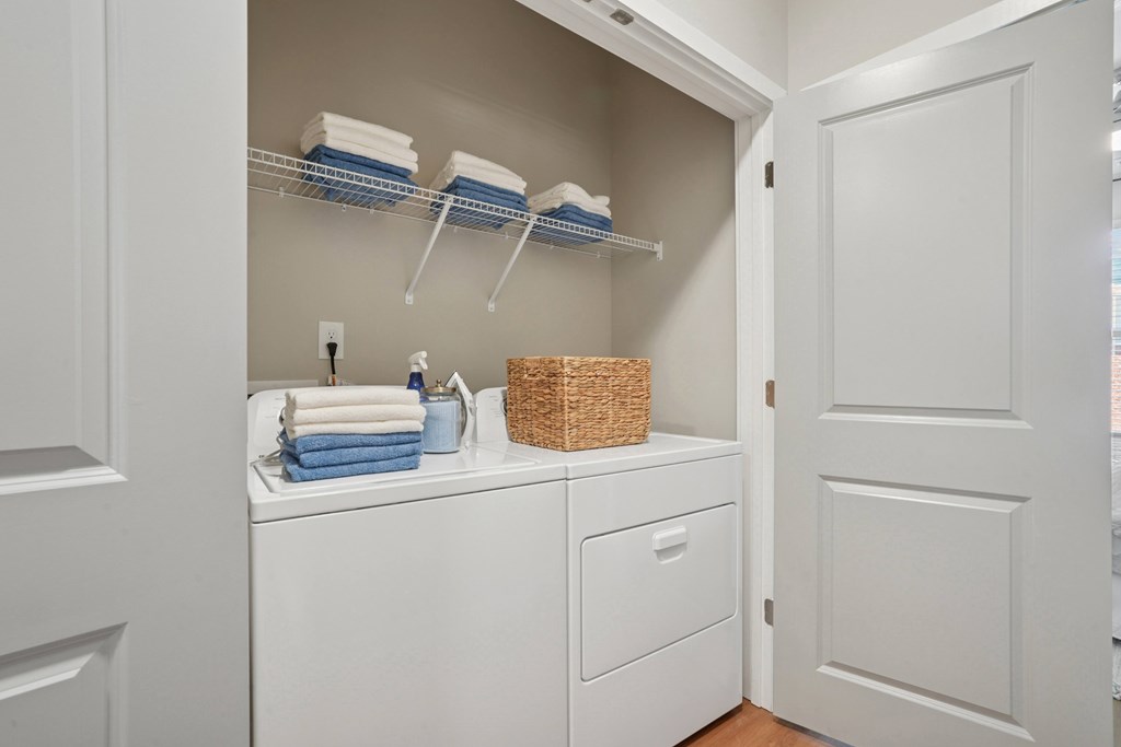 A white laundry room with a washer and dryer, a basket, and towels.