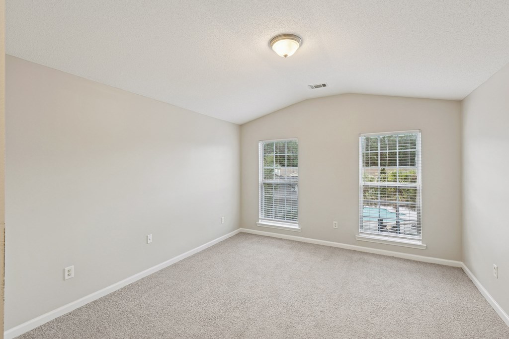 A spacious room with carpeted floor and two windows.