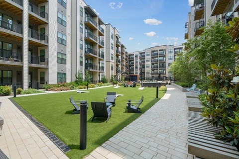 an outdoor lounge area with chairs and tables on a lawn in front of an apartment building