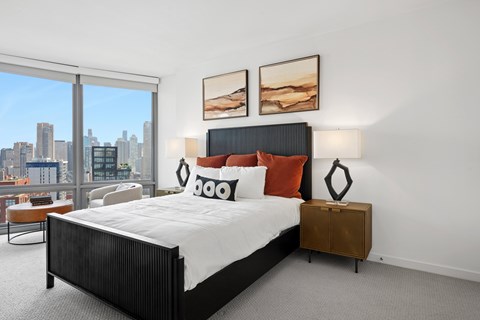 A bedroom with a large bed and a city view through the window.