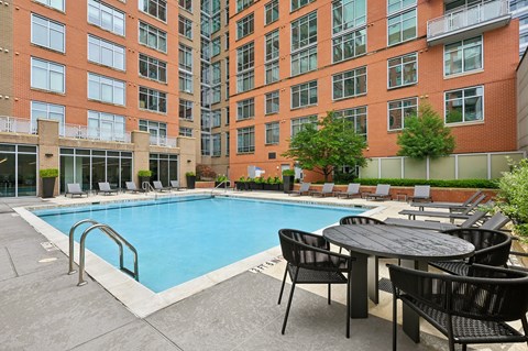A pool surrounded by chairs and tables in front of a brick building.
