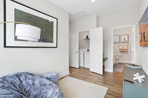 A bedroom with a bed covered in a blue blanket and a white lamp on the wall.