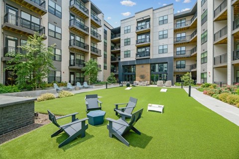 an outdoor lounge area with chairs on a lawn in front of an apartment building