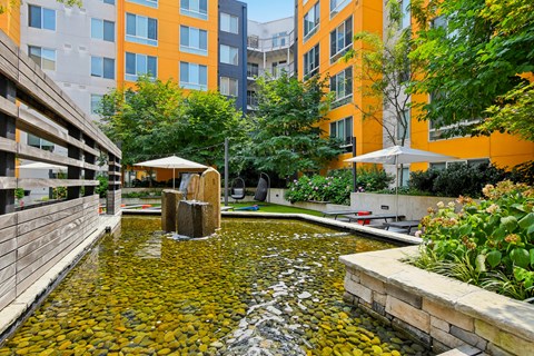 A small pond with a waterfall in the middle of a courtyard surrounded by buildings.