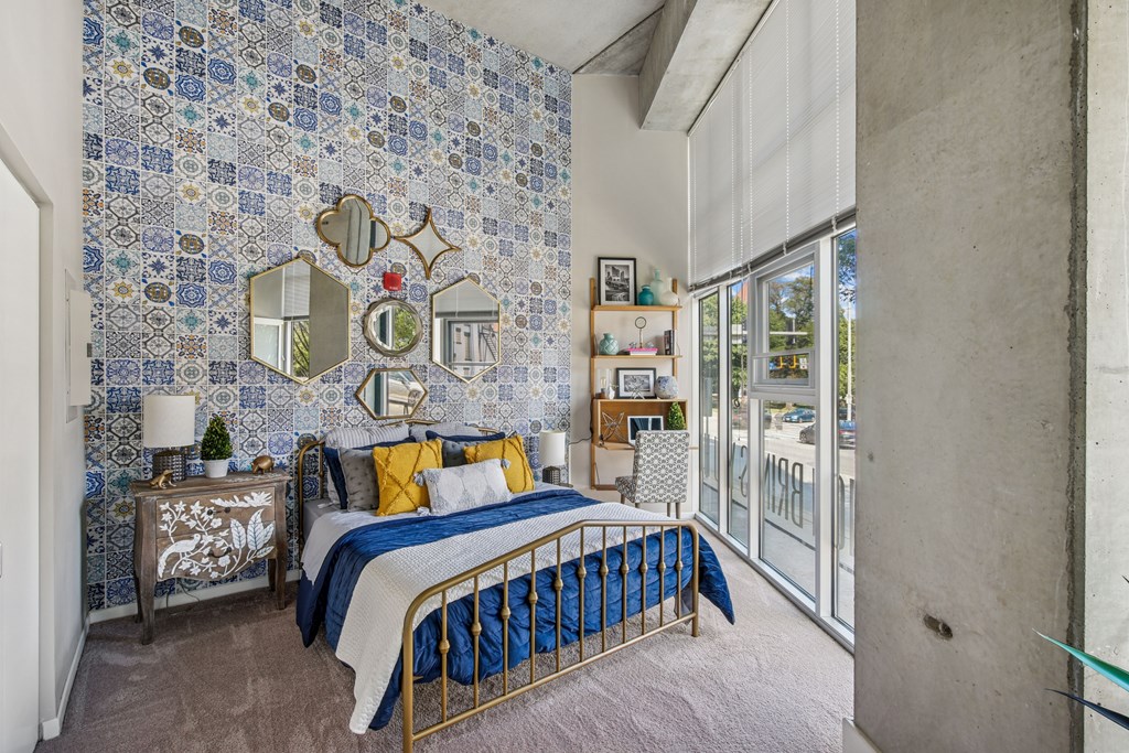 A bedroom with a bed, nightstand, and a wall covered in blue and white tiles.