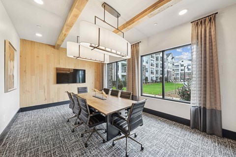 A conference room with a long table and chairs, a television, and a view of the outside.