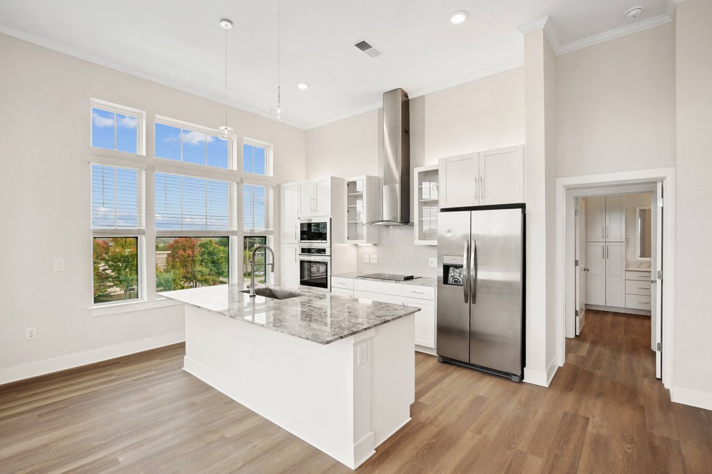 a white kitchen with a large island and a stainless steel refrigerator