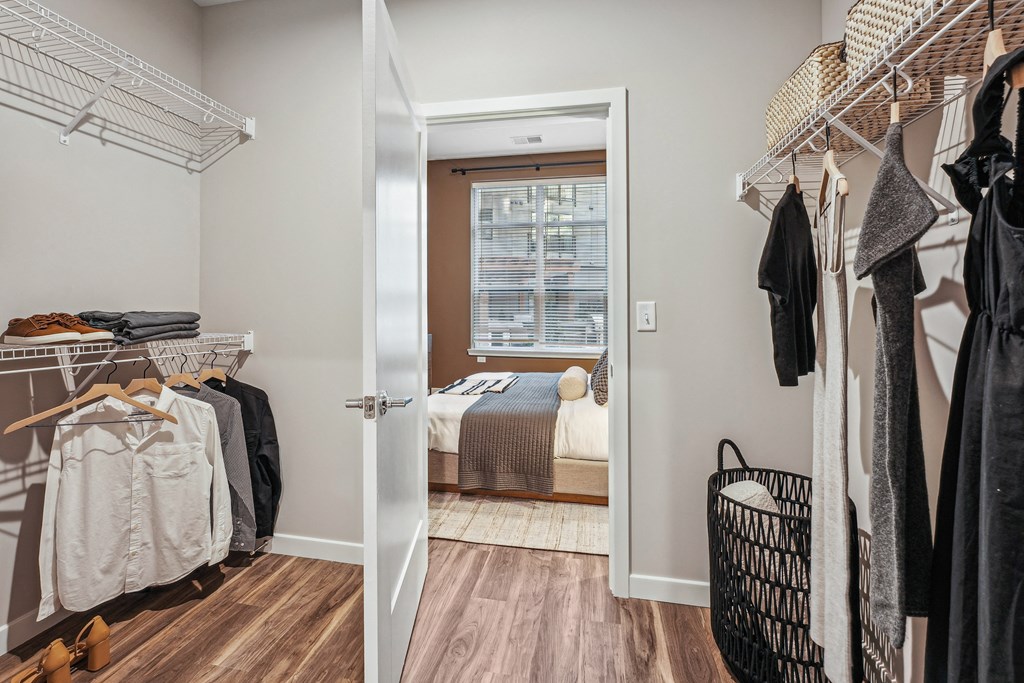 a walk in closet with clothes hanging on a rack and a bedroom in the background