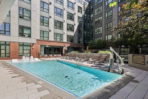 A swimming pool surrounded by a brick wall and lounge chairs.