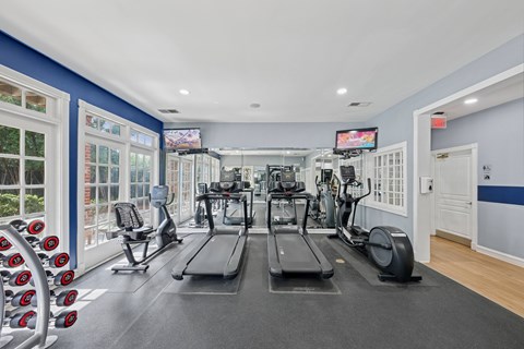 A gym with treadmills, elliptical machines, and dumbbells.
