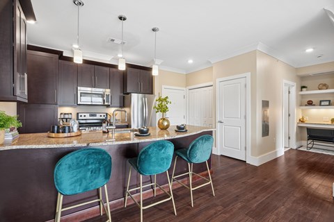 A kitchen with dark brown cabinets and a bar area with green bar stools.