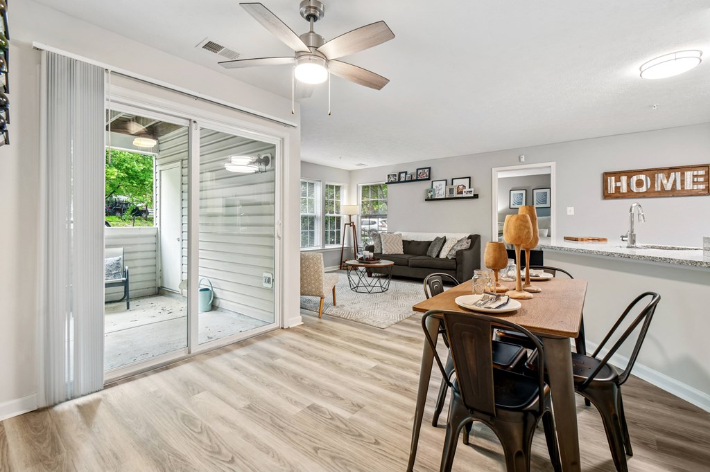 A dining room with a table set for two and a sliding glass door leading to a backyard.