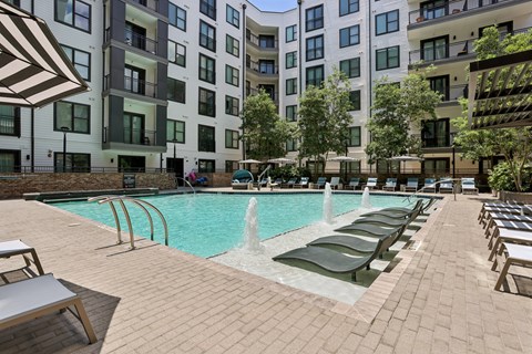 A pool with a waterfall and lounge chairs in front of a building.
