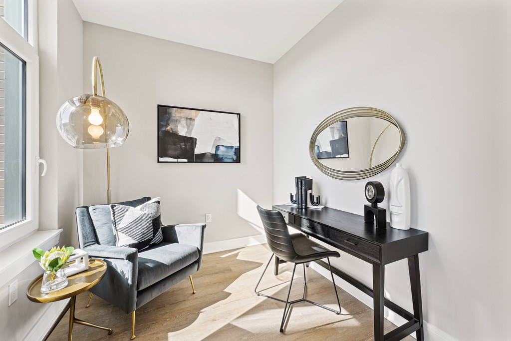 A modern living room with a grey couch, a black desk, and a round mirror.