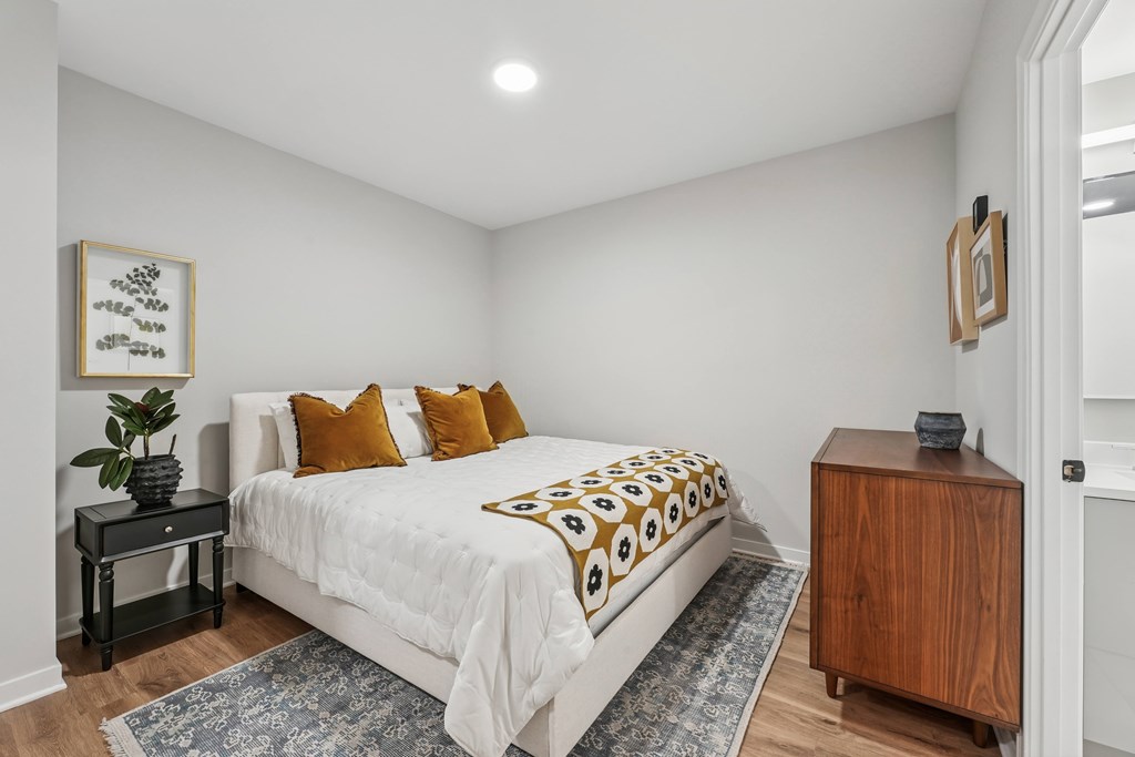 A bedroom with a bed, nightstand, and a plant.