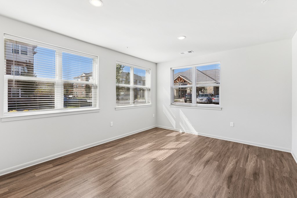 A room with wooden flooring and two windows.