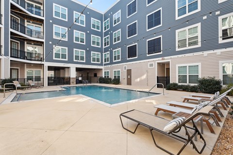 A swimming pool surrounded by lounge chairs in front of apartment buildings.