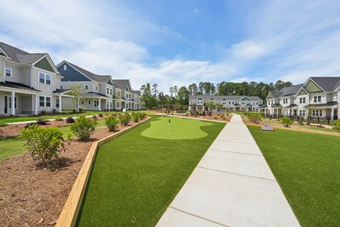 A long concrete walkway leads through a grassy area in front of apartment buildings.