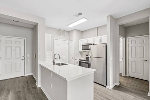 a white kitchen with a large island and stainless steel refrigerator