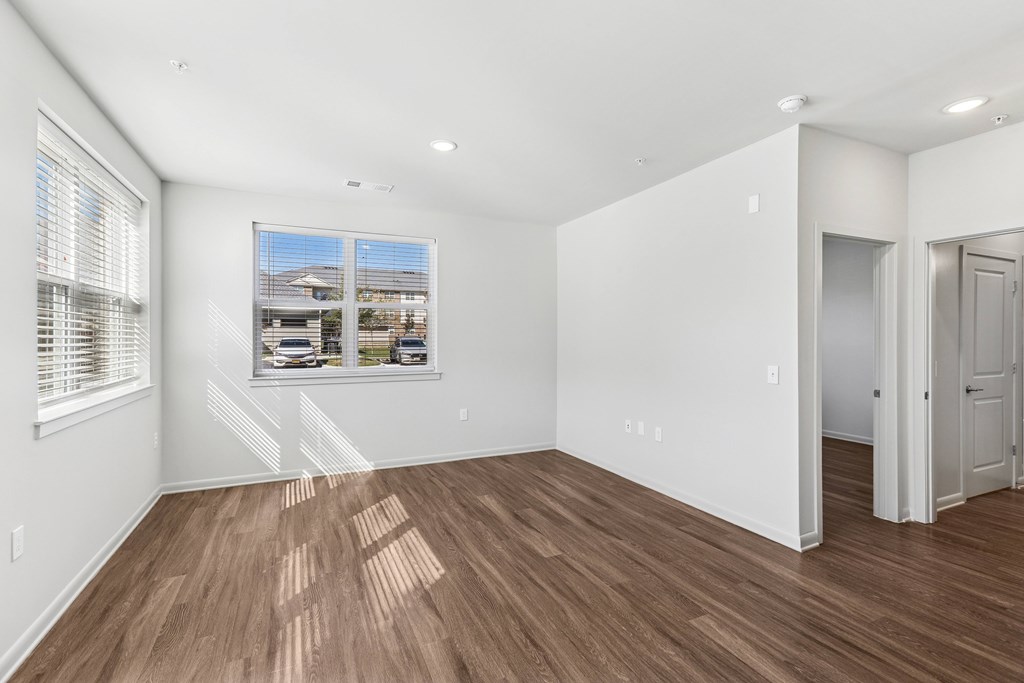 A room with white walls and wooden flooring with a window.