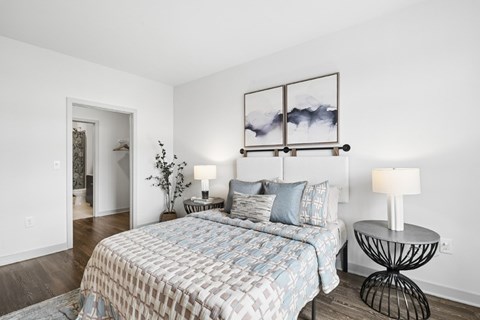 A bedroom with a bed, a side table with a lamp, and a picture frame on the wall.
