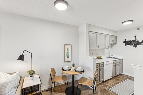 A kitchen with a table and chairs in the foreground and a countertop with a sink in the background.