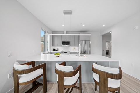A modern kitchen with white cabinets and a large island with chairs.