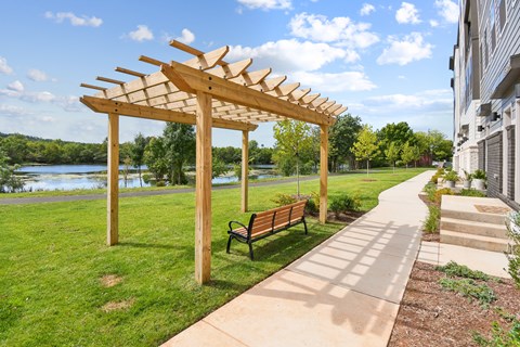 A wooden pergola with a bench is situated on a concrete pathway.