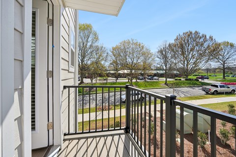A balcony with a black railing and a view of a parking lot and trees.