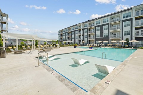 A large swimming pool with lounge chairs and umbrellas in front of apartment buildings.
