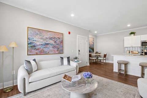 A living room with a white couch and a painting on the wall.