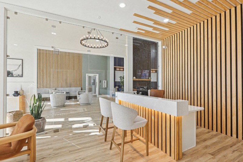 A reception area with a white counter and wooden chairs.