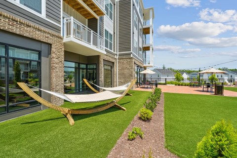 A modern building with a balcony and a hammock on the lawn.