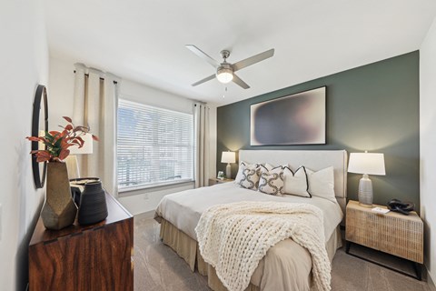A bedroom with a bed, a ceiling fan, and a window with blinds.