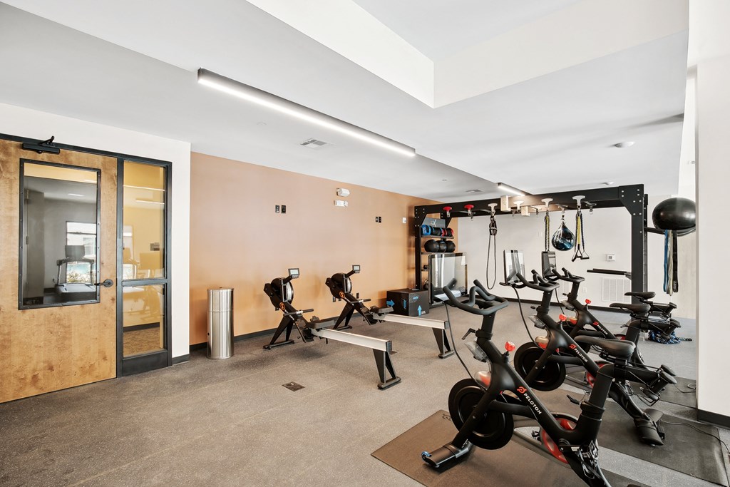 a gym with various bikes and weights on the floor and a glass door