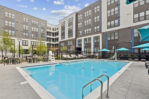 A swimming pool in front of a building with a blue umbrella.