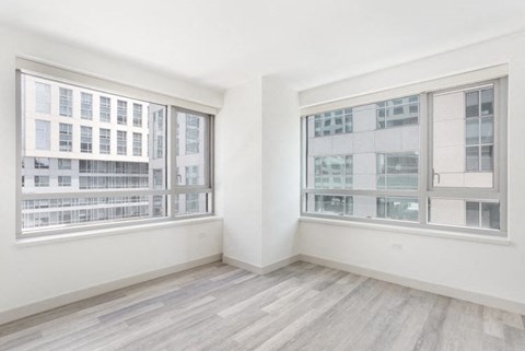 a bedroom with two large windows and hardwood floors