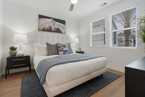 A bedroom with a large bed, a painting of a horse, and a ceiling fan.