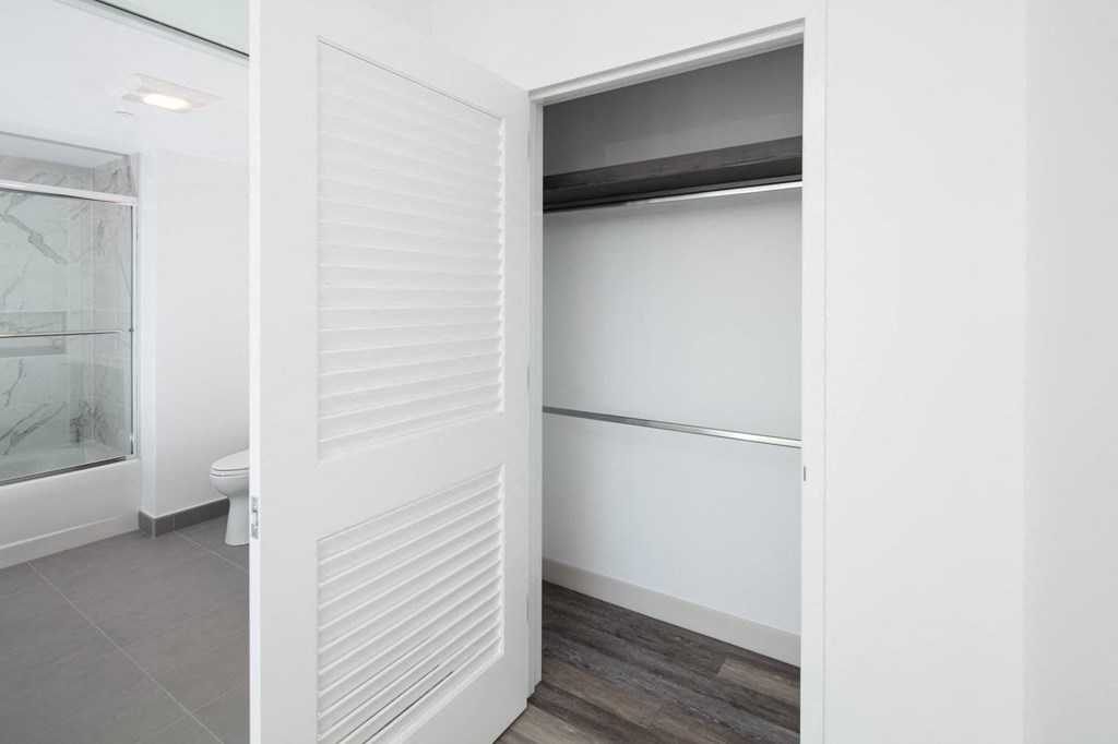 a walk in closet in a bedroom with white walls and a wooden floor