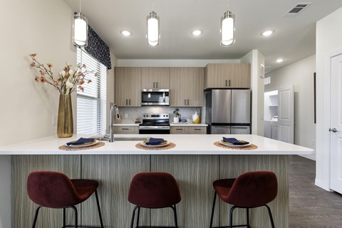 A modern kitchen with a bar area and red chairs.